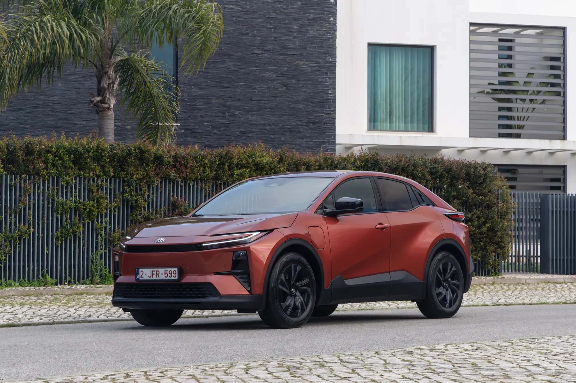 Le Toyota C-HR+ cuivre vu de trois quarts avant devant une maison contemporaine