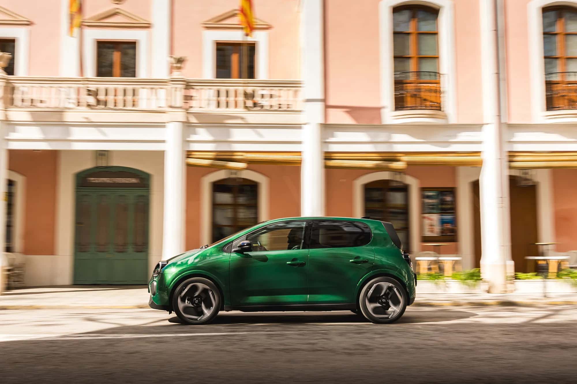 Renault Twingo E-Tech Techno 2026 en Vert Absolu, vue de profil en roulage devant une façade urbaine