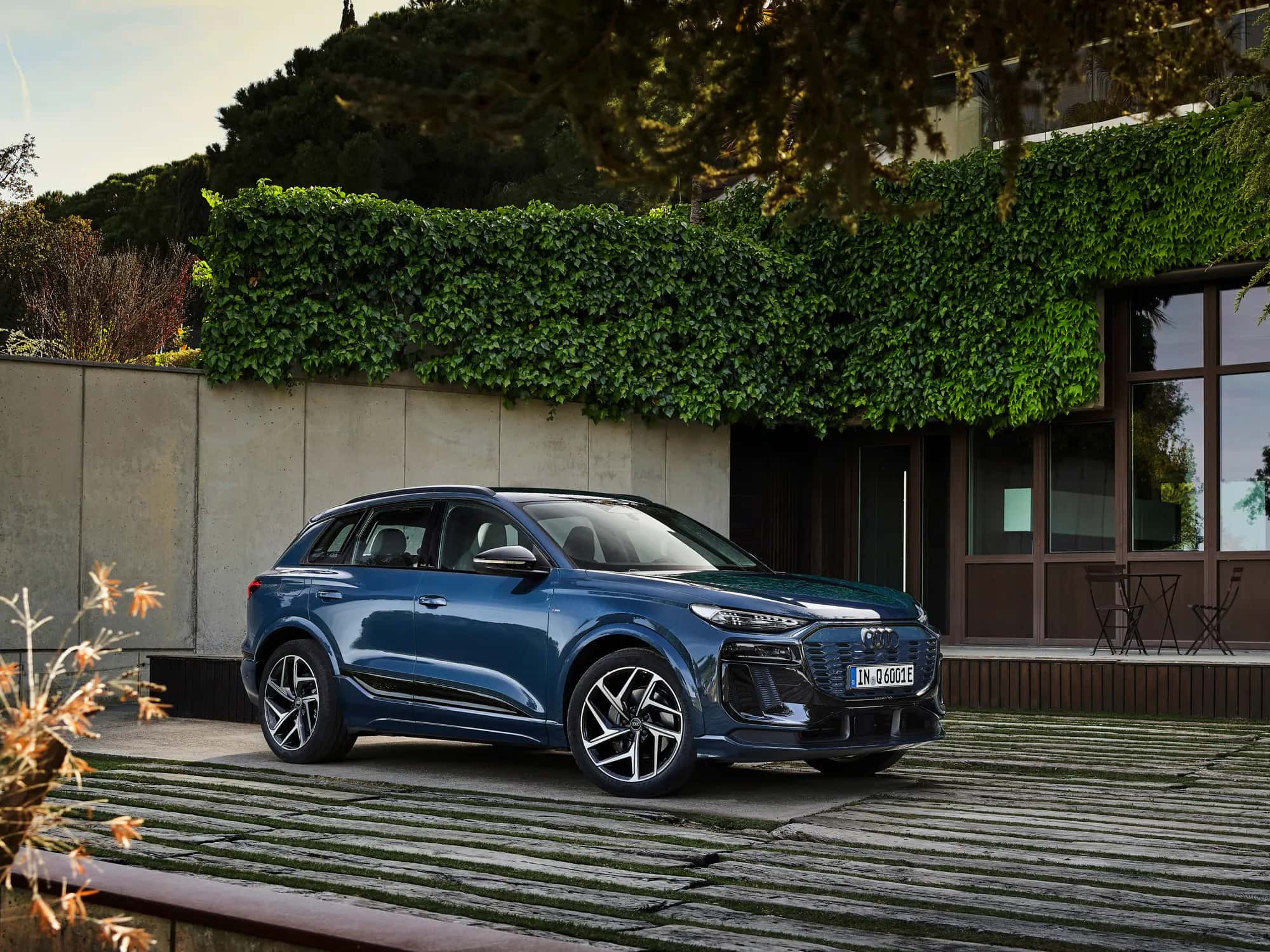 L'Audi Q6 e-tron bleue vue de trois quarts avant devant une maison contemporaine