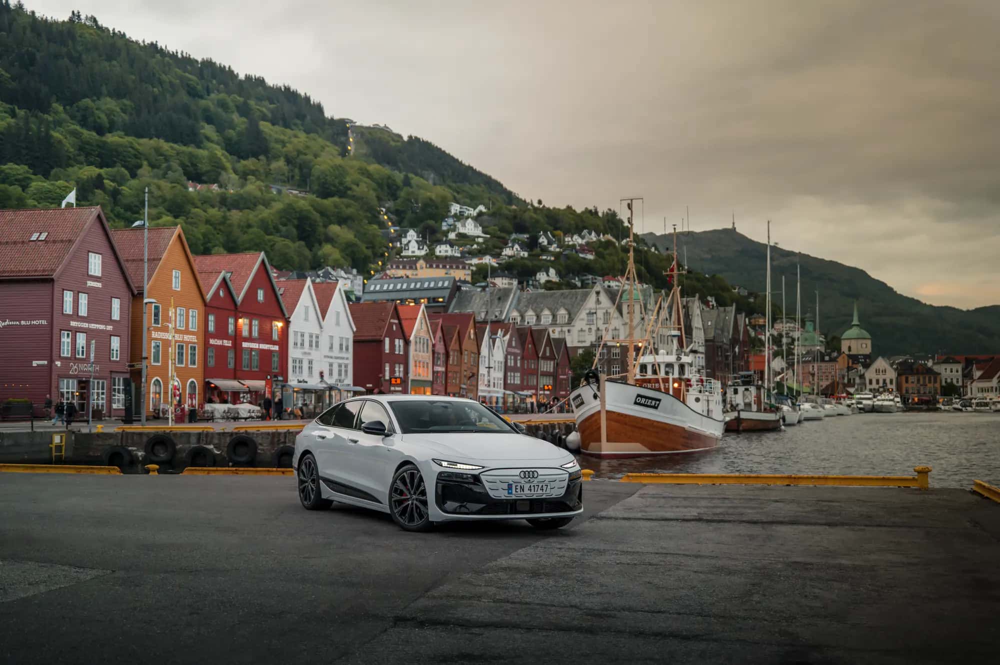 L'Audi A6 Sportback e-tron blanche vue de trois quarts avant, sur un quai bordé de maisons colorées