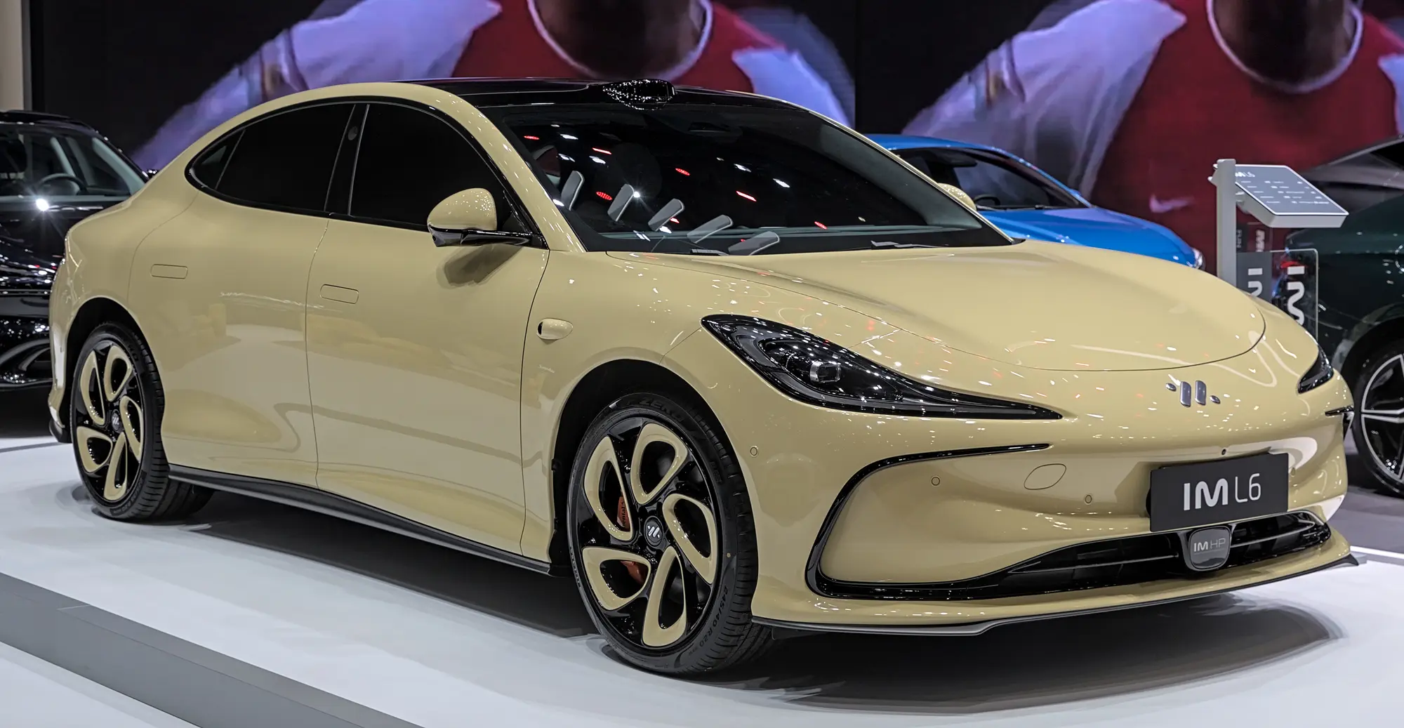 La berline MG IM5 beige vue de trois quarts avant sur un stand de salon