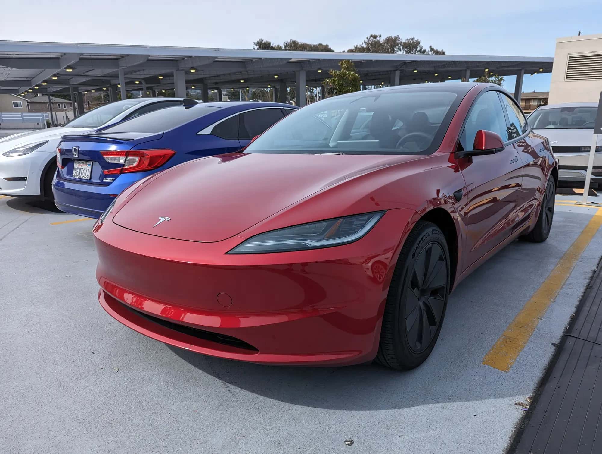 Une Tesla Model 3 rouge vue de trois quarts avant dans un parking