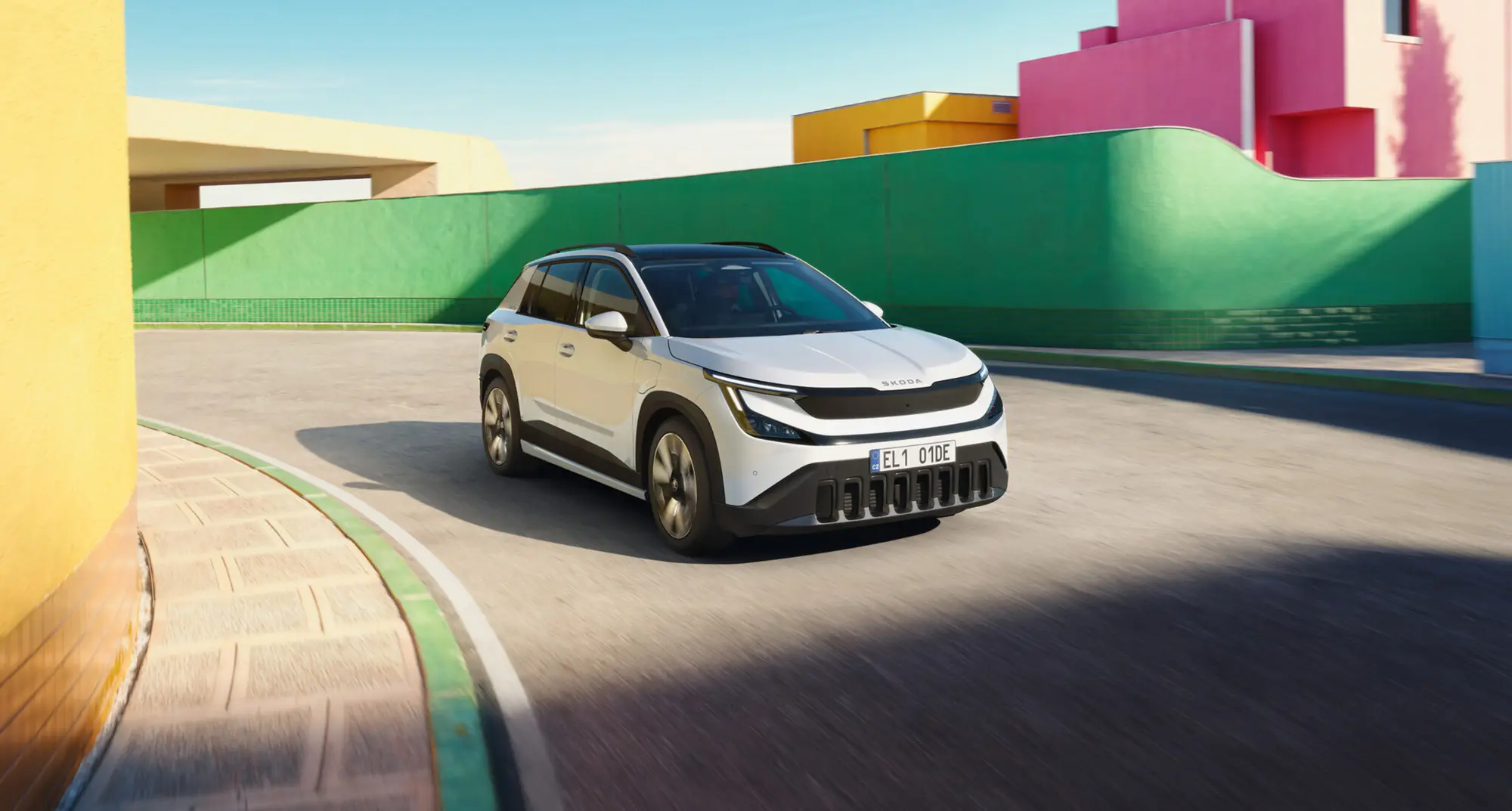 Le Škoda Epiq blanc à toit noir, vu de trois quarts avant en mouvement sur une voie urbaine bordée de murs colorés