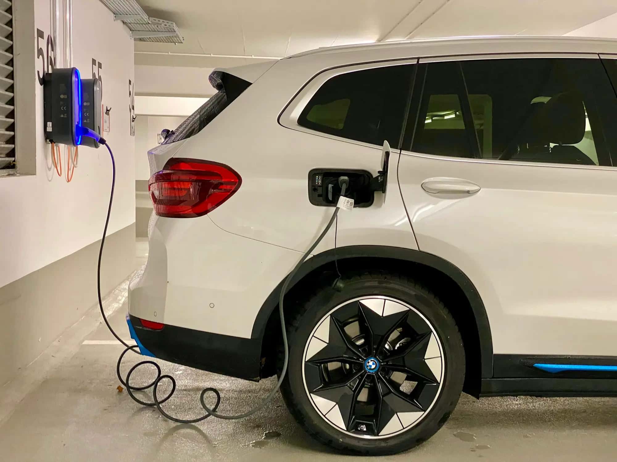 Une voiture électrique blanche branchée à une borne murale dans un parking couvert