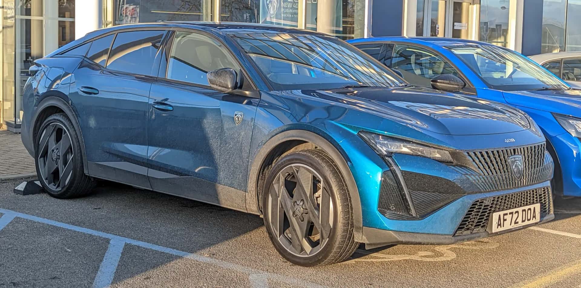 Peugeot 408 bleue vue de trois quarts avant sur un parking, la carrosserie que partage la version électrique e-408