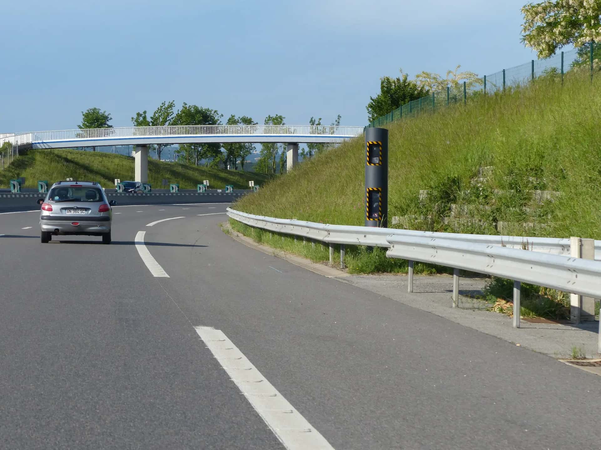Un véhicule gris passe devant un radar automatique dressé au bord d'une autoroute