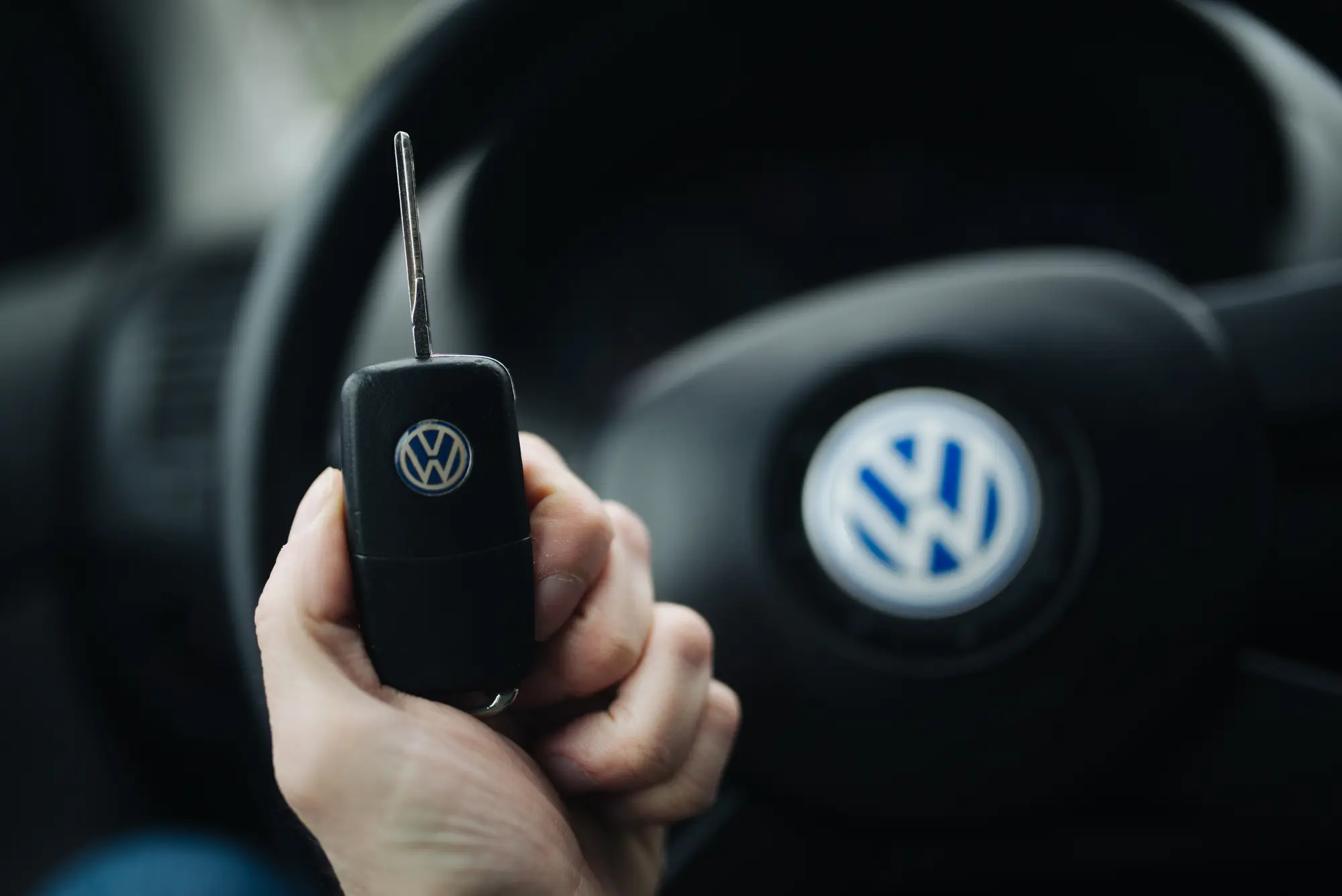 Une main tient une clé de voiture devant un volant flou, à l'intérieur d'un véhicule