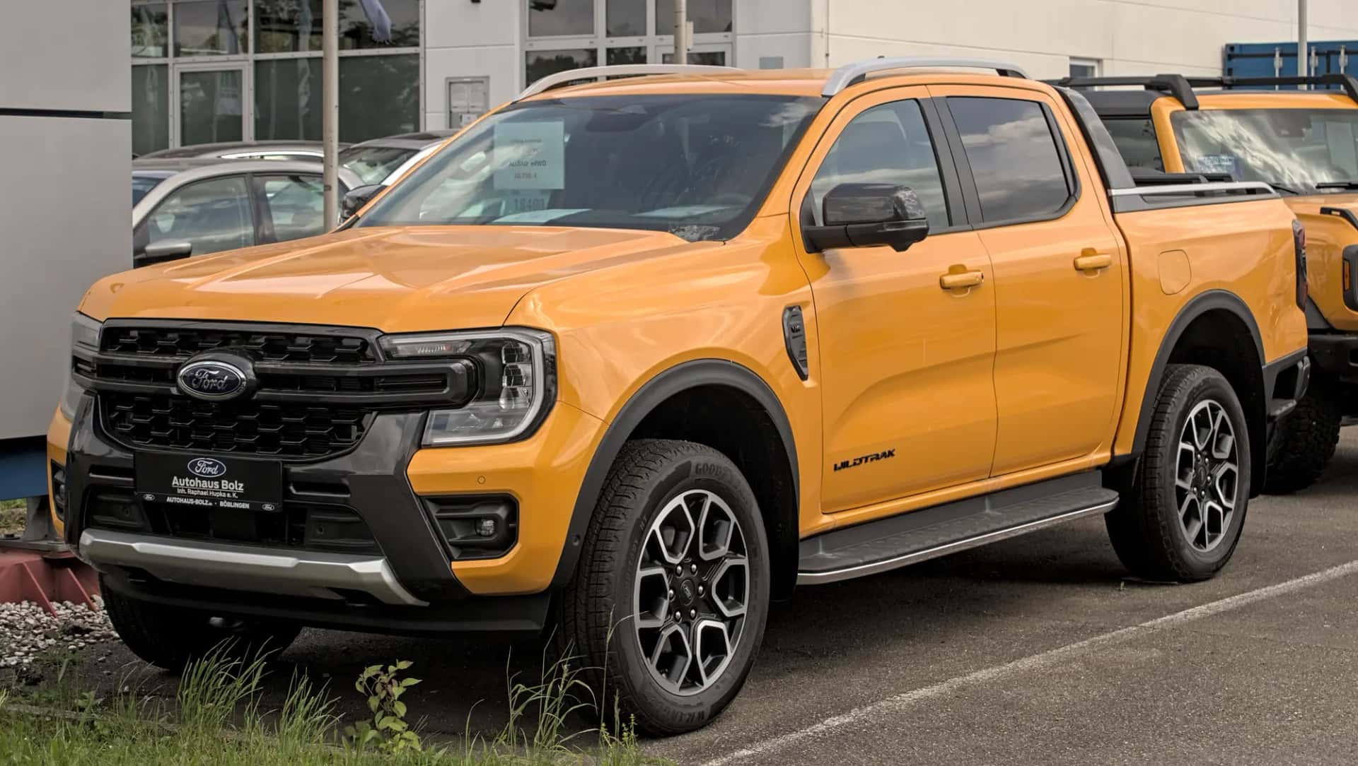 Un pick-up double cabine orange à quatre portes, garé sur un parc, vu de trois quarts avant