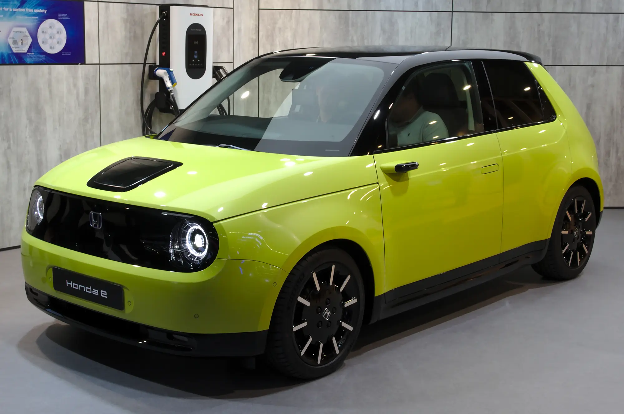 Une petite voiture électrique vert citron branchée à une borne de recharge murale