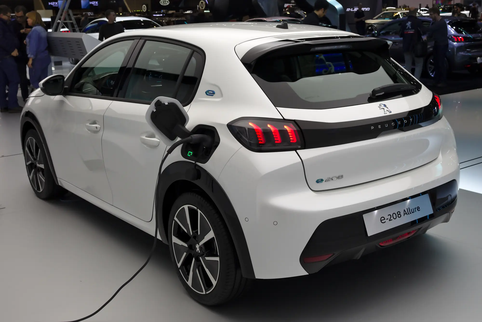 Une citadine électrique blanche branchée par un câble de recharge, vue de trois quarts arrière